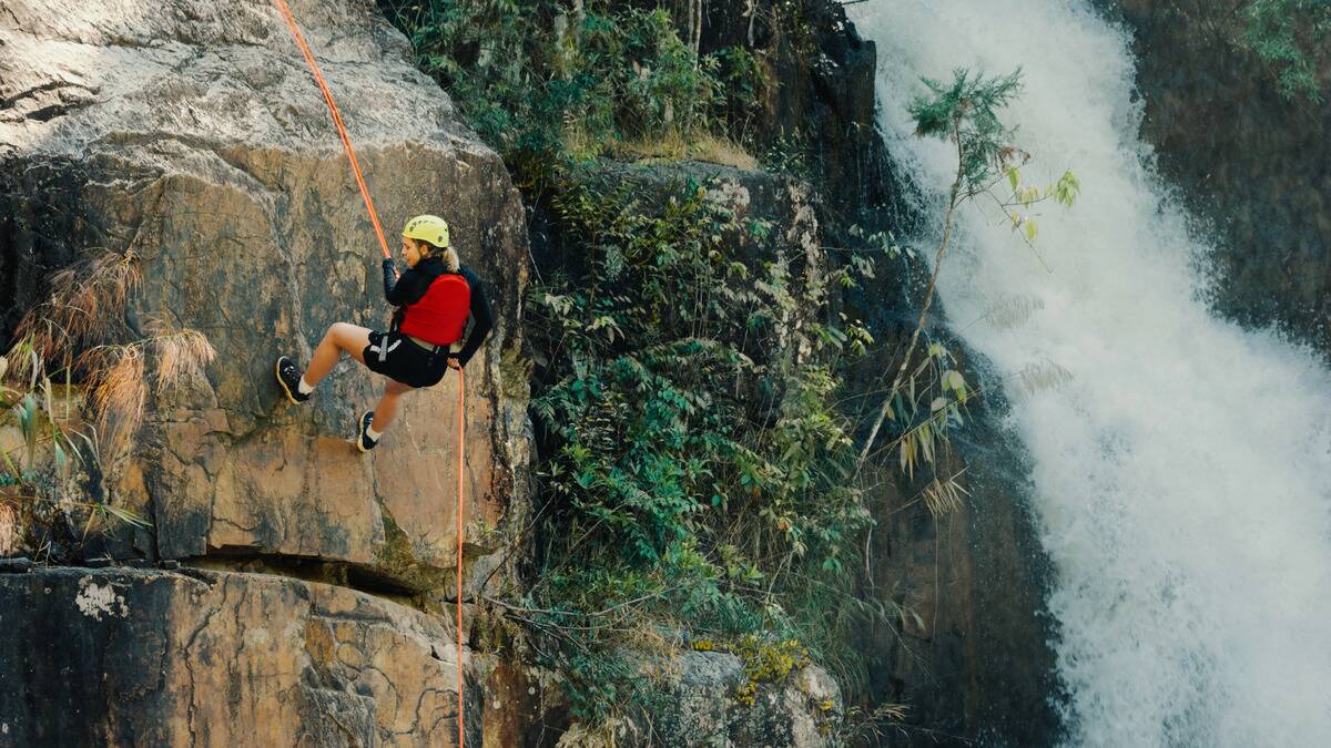 A woman scaling down a cliff face next to a waterfall.