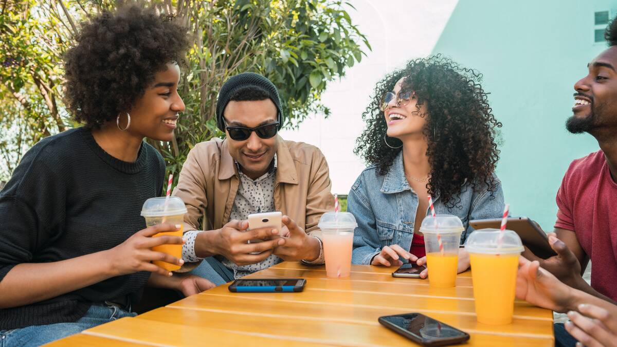 A group of friends sitting around a cafe table with drinks, smiling and laughing as they chat.