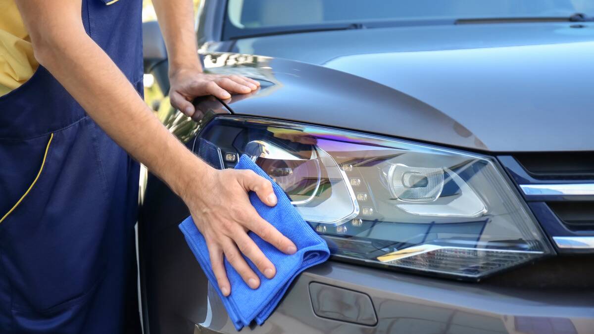 A close shot of a hand wiping down a car headlight with a microfiber cloth.