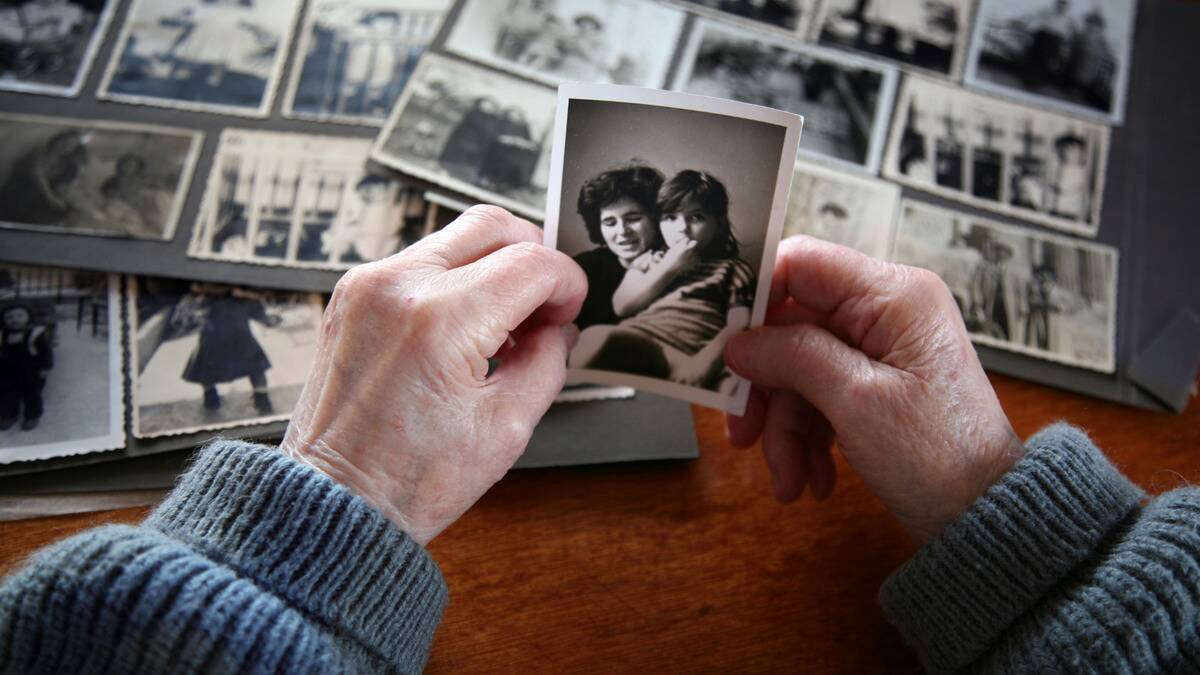 A pair of hands holding a black-and-white family photo, an album of others photos on the table beneath.