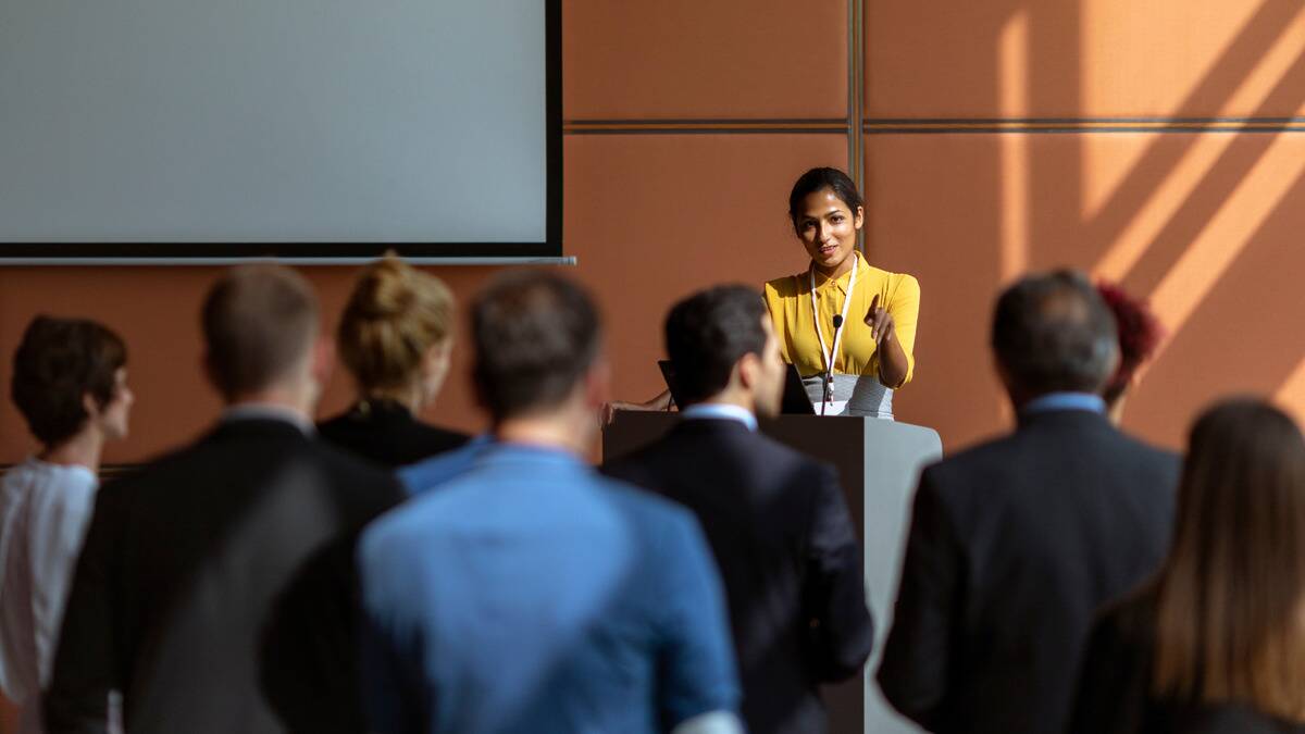 A woman standing at a podium, speaking to a group of people during a presentation.