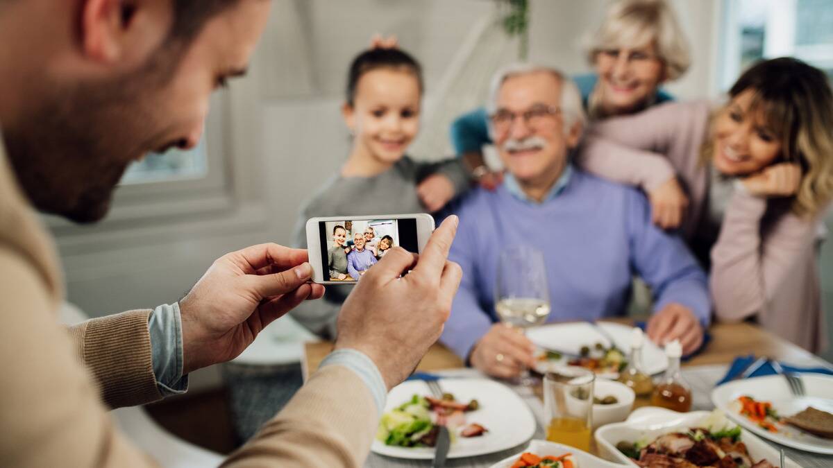 A man taking a photo with his phone of the rest of his family gathered up together, all smiling.