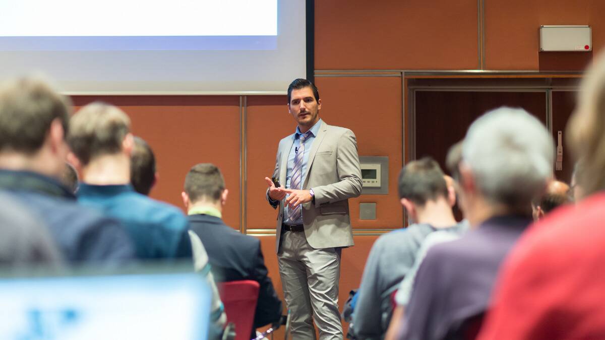 A business man standing in front of a crowd, giving a presentation.