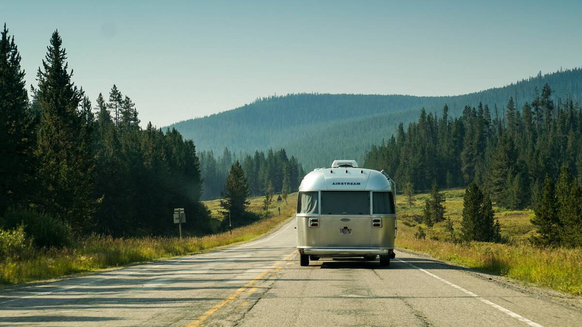 A trailer being towed down a long road surrounded by trees and hills.