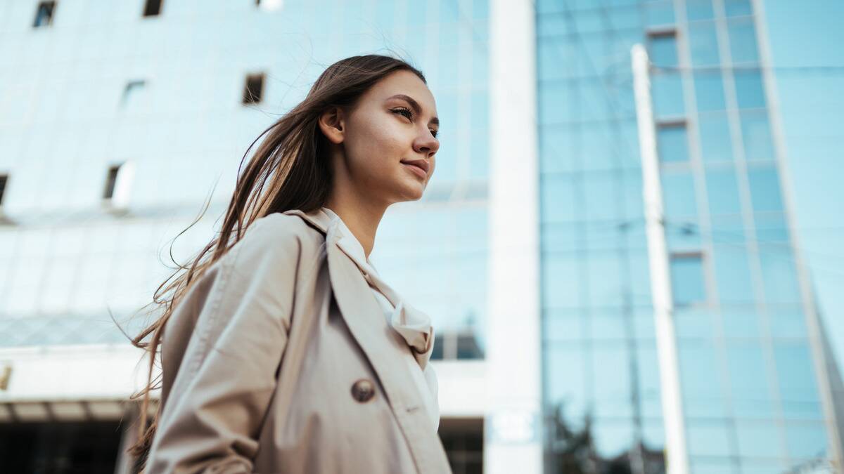 A low angle shot of a woman walking through a city street, looking forward confidently.