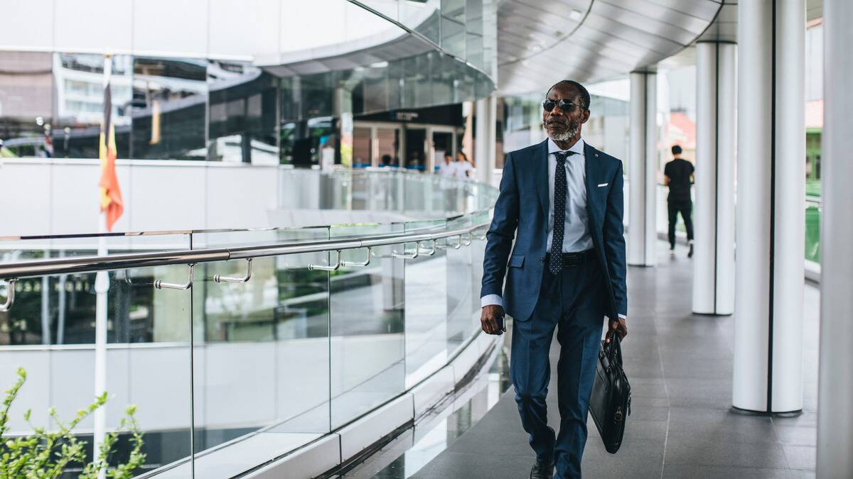 A business man in a suit and sunglasses walking confidently through a building.