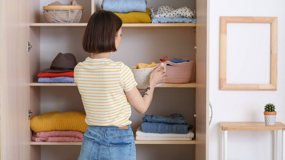 A woman facing away from the camera is organizing her closet, putting some clothes in baskets.