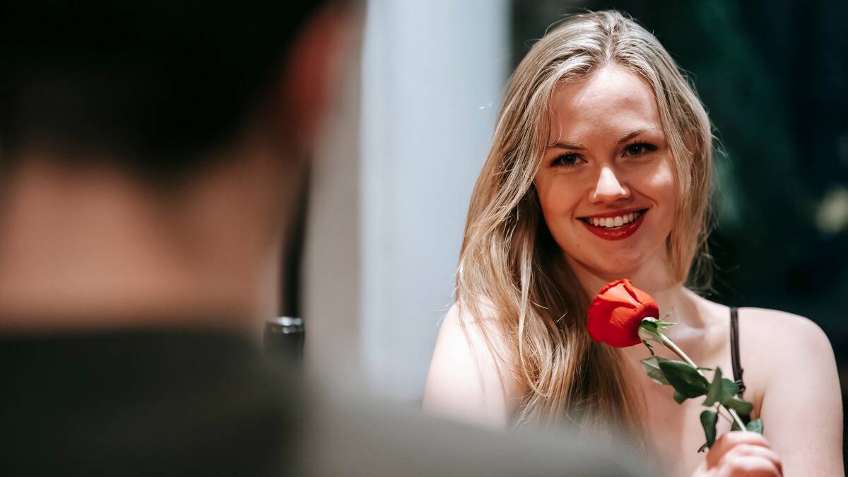 An over the shoulder shot showing a woman smiling after a man just handed her a rose.