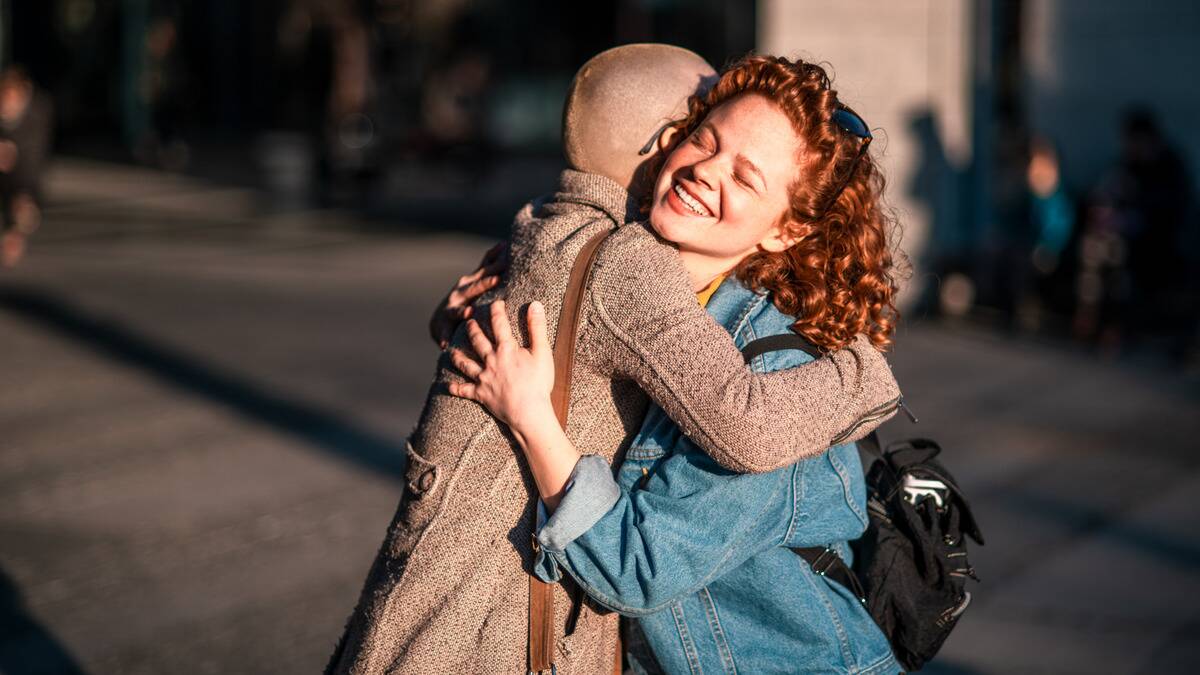 Two friends hugging happily as they stand in the sunshine.