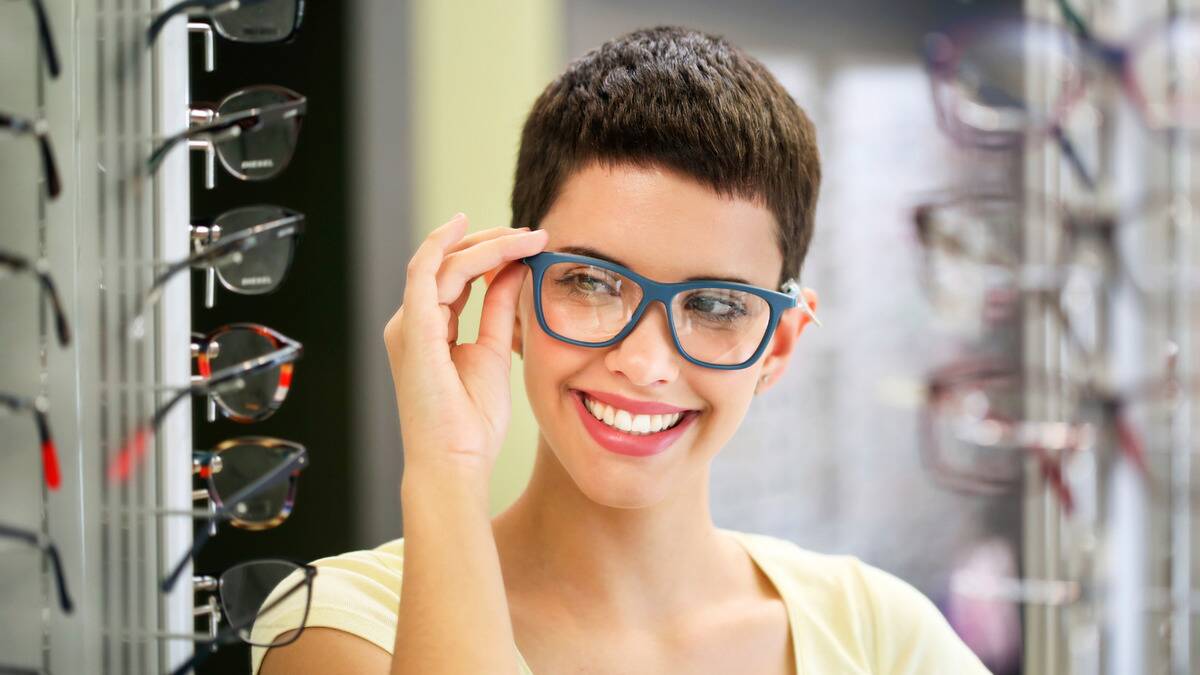 A woman shopping for glasses, trying out new frames in the mirror.