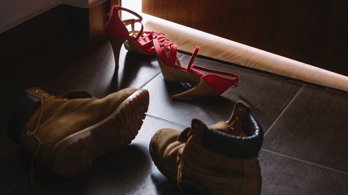 A pair of high heels and a pair of work boots discarded just outside of a slightly open door.