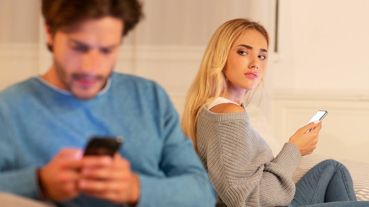 A woman looking over her shoulder at her boyfriend, who's looking down at his phone.