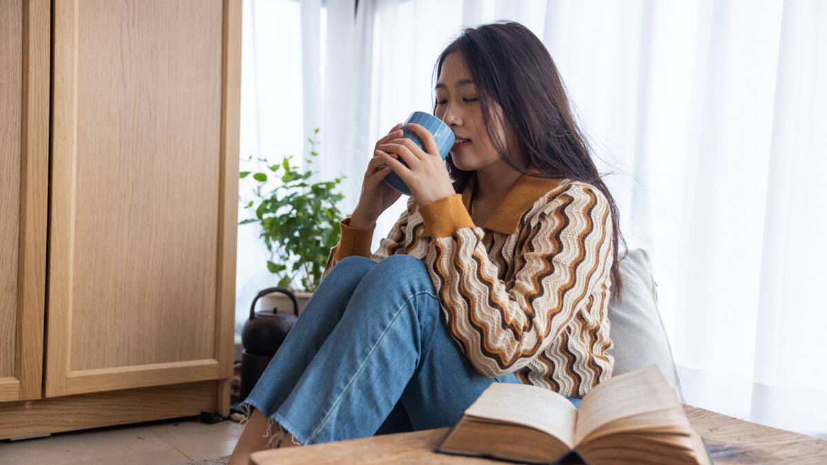 A woman sitting at home on the floor, drinking from a mug peacefully.