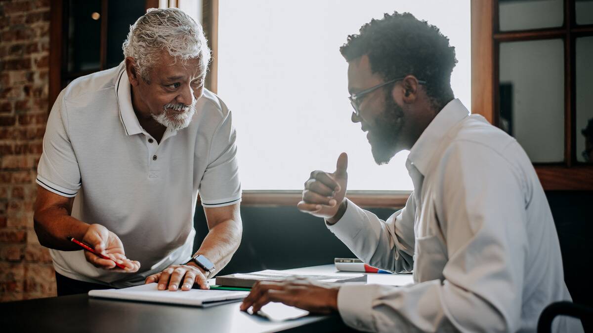 A father and his son sitting across from each other at a table, the father seeming to question something his son is saying.