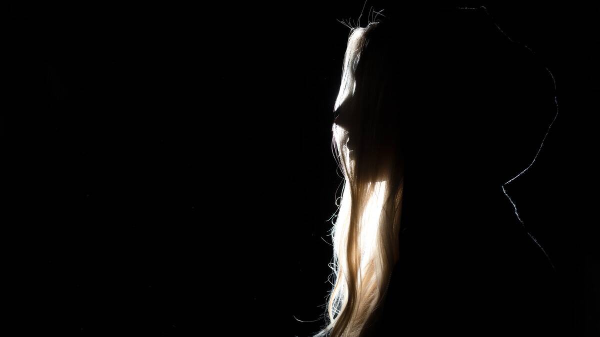 A woman in the dark, only her hair and the silhouette of her face in profile able to be seen.