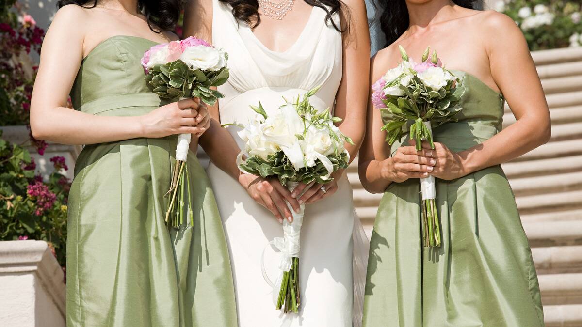 A torso shot of a bride standing between two of her bridesmaids who are in sage green dresses, each holding a bouquet.