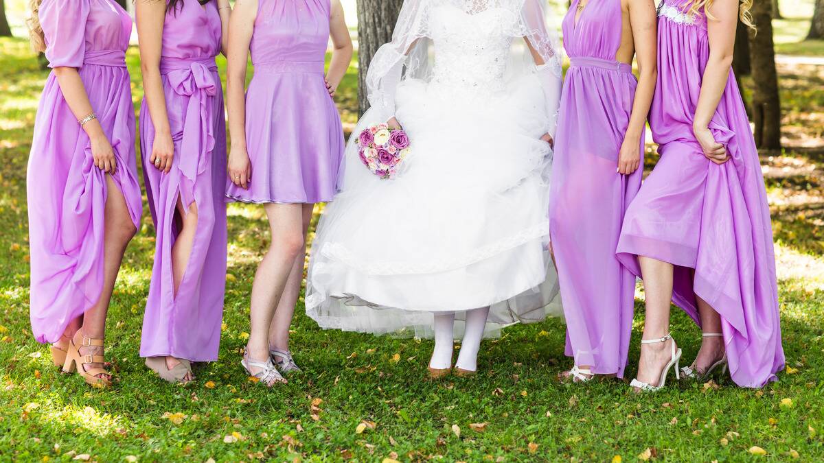 A neck-down photo of a bride standing in the middle of her bridesmaids who are all in pink-purple dresses of different styles, but the same color.