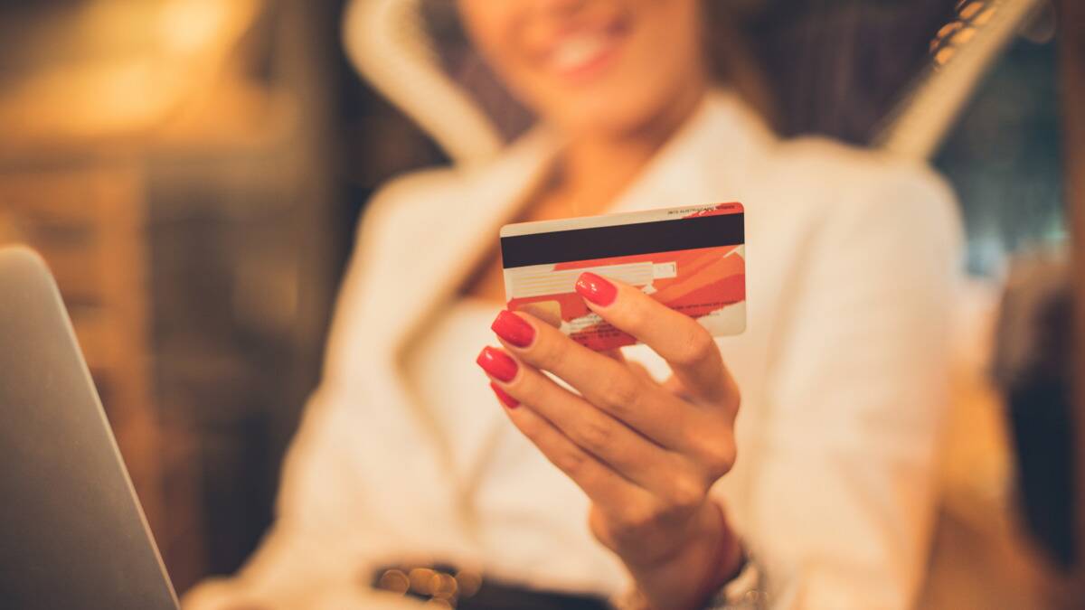 A woman holding up her credit card, smile visible in the background.