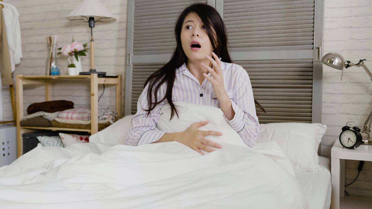 A woman sitting up in bed looking shocked, seeming to have just woken up from a bad dream.