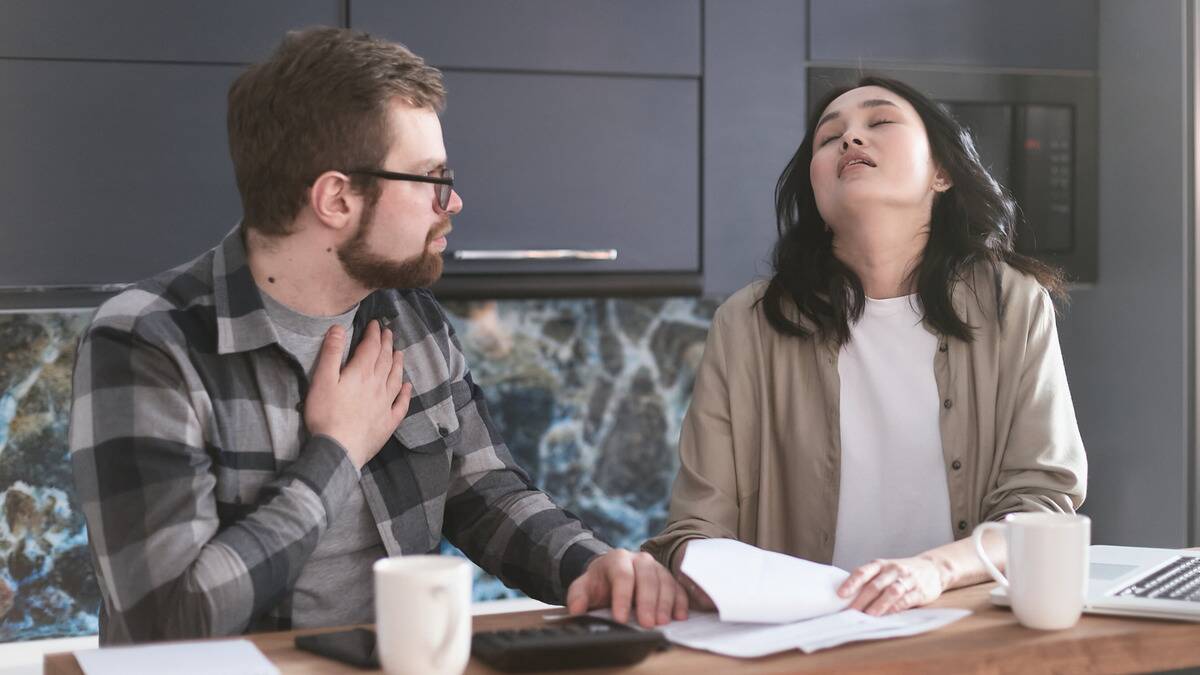 A couple sitting together at a table, the woman looking bored, the man looking hurt.