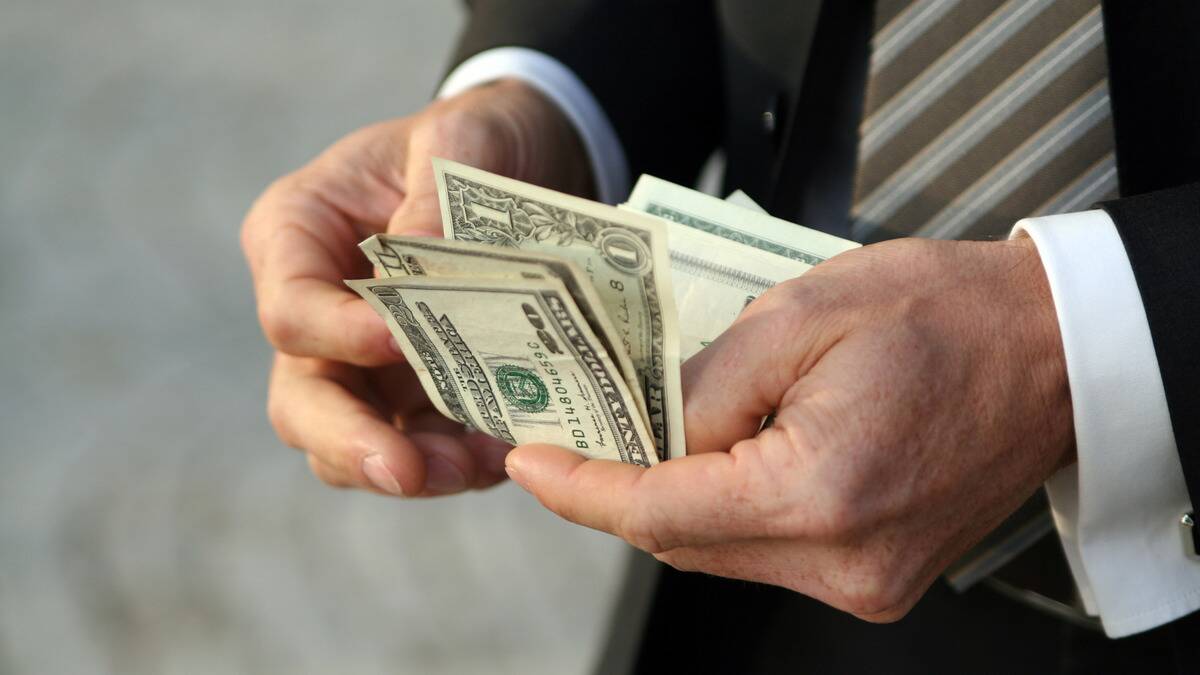 A close shot of a pair of hands counting through a small bundle of various currency bills.