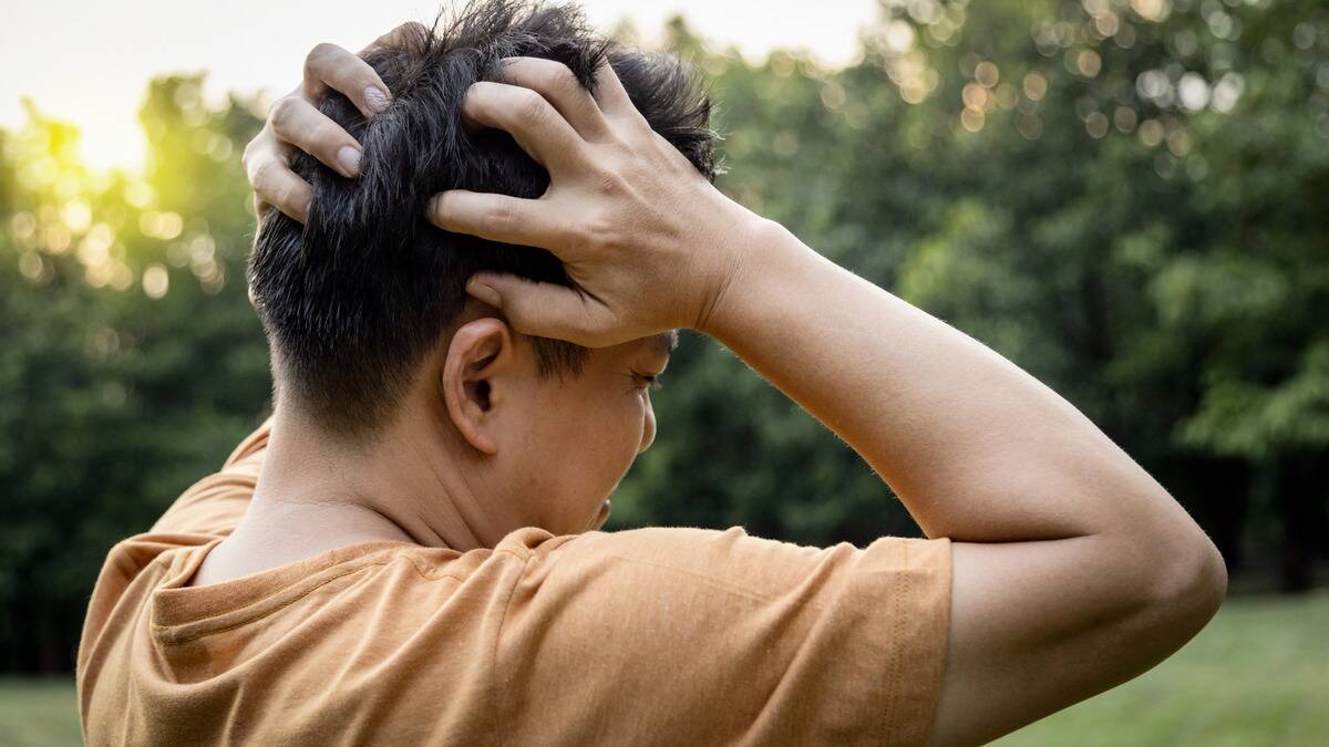 A man facing away from the camera, gripping his head in stress.