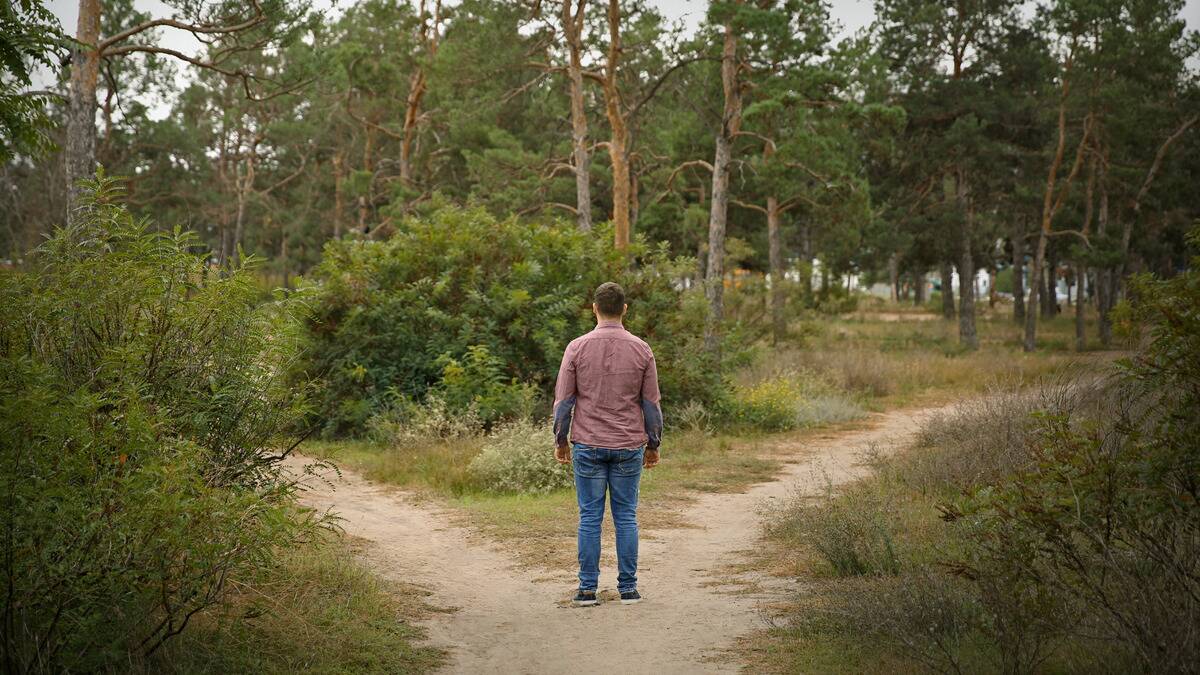 A man stands at a fork in the path he's walking, staring down both options.