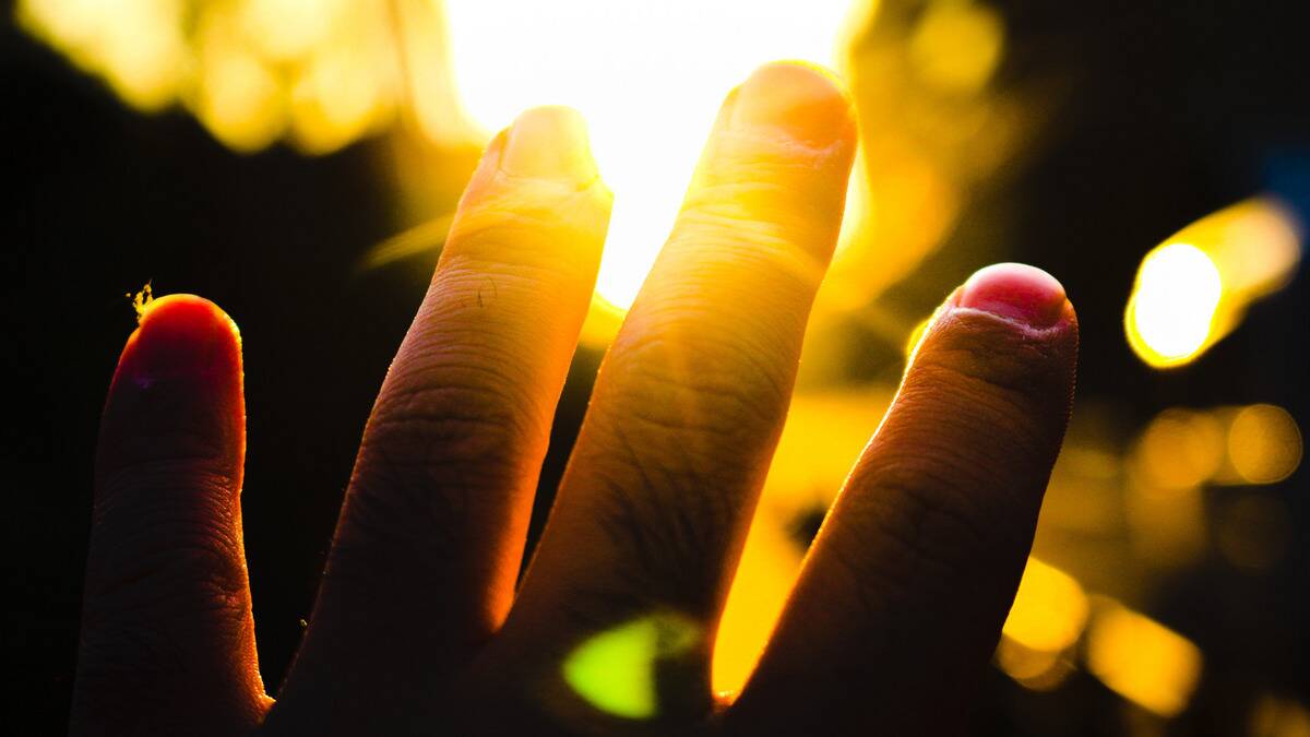 A close shot of someone's hand as they reach out toward the sun, the light shining through their fingers.