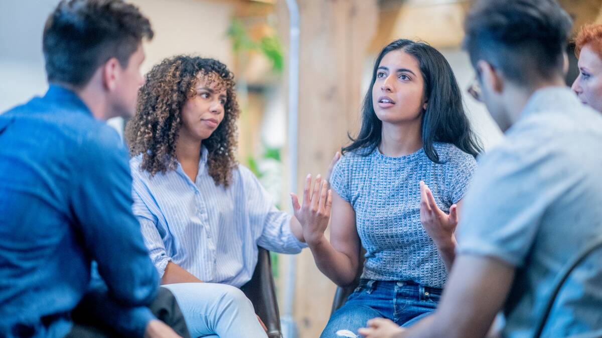 A woman speaking in a group therapy session, the woman next to her putting a comforting hand on her shoulder.