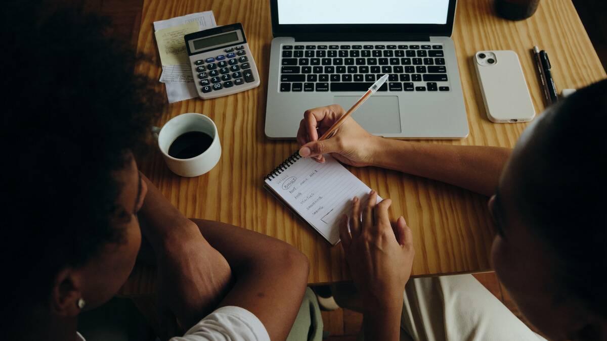 An over-the-shoulder shot of a couple plotting out their financial budget together. 