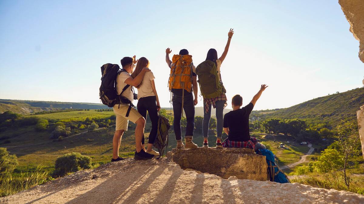 A group of friends out for a hike, standing together at the peak of their walk, arms in the air.