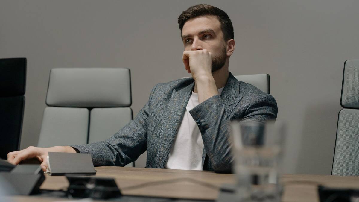 A man sitting at a board room table, looking to be thinking seriously about something.