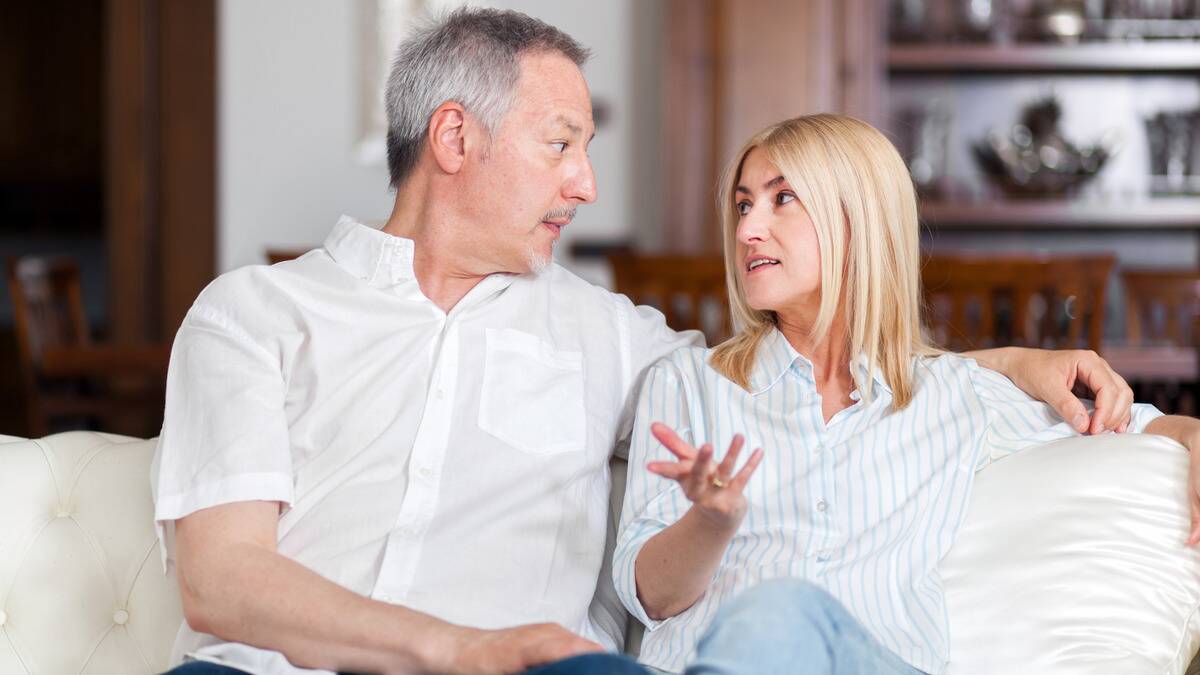 A couple sitting side by side on a couch, seeming to be talking about something seriously.