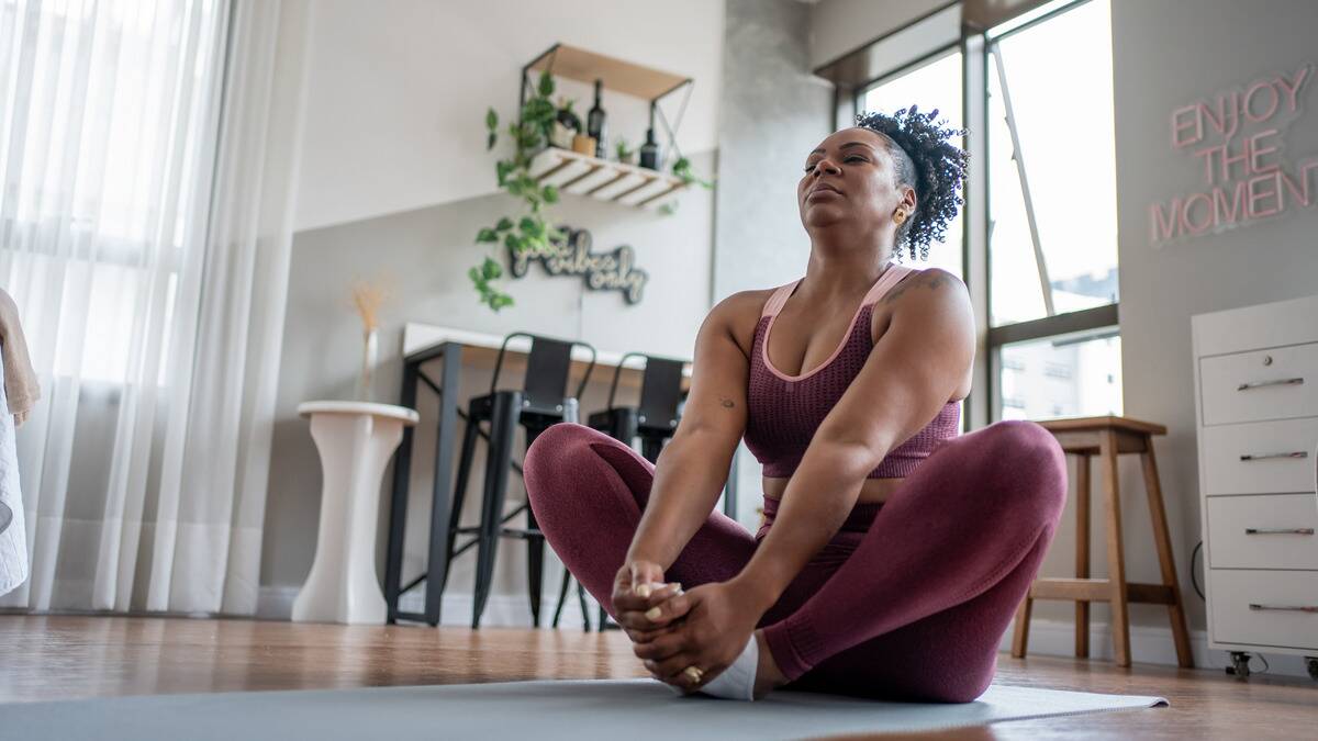 A low-angle shot of a woman doing yoga, currently in butterfly pose with her eyes closed.