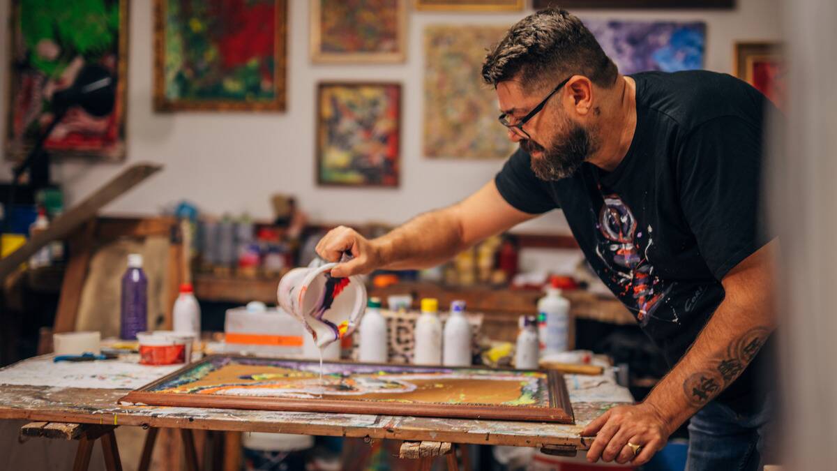 A man leaning over his work table doing acrylic pour style art.