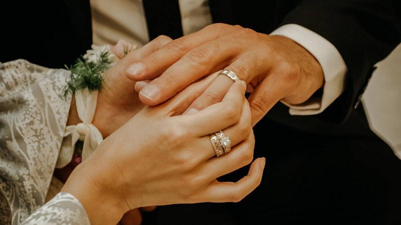 A close shot of a pair of hands getting married, the bride putting the ring on her groom's finger.