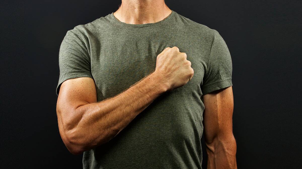 A torso shot of a man holding one hand in a fist over his heart.