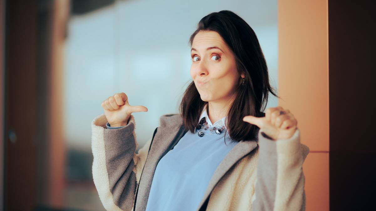 A woman with a smug expression pointing at herself with both of her thumbs.