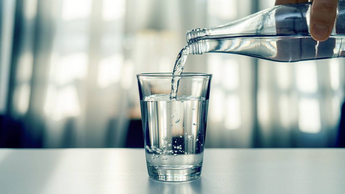 Someone pouring water from a small glass bottle into a glass cup.