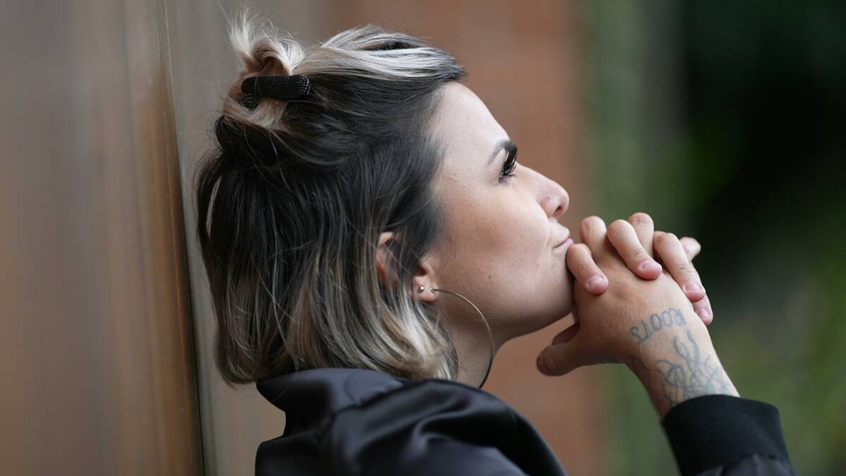 A close shot of a woman sitting outside, shot in profile, hands crossed against her chin as she looks up at the sky.