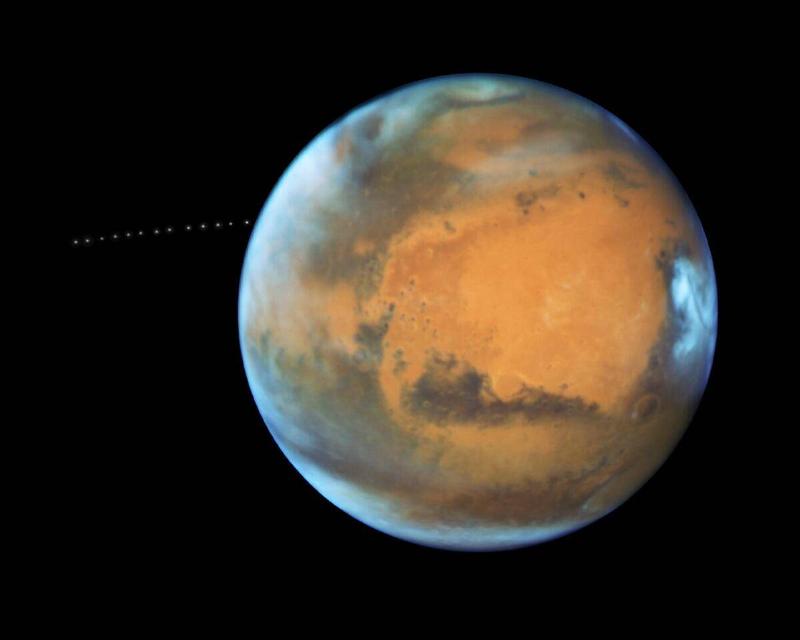 A long-exposure shot of Mars from the Hubble telescope, its moon's, Phobos, path of travel behind it.