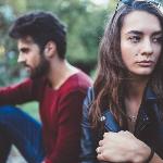 A man and woman sitting next to each other but facing away one another, the focus on the woman who's looking to the side sadly.