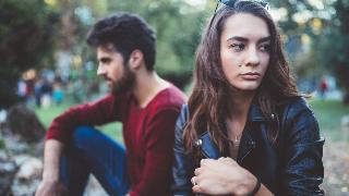 A man and woman sitting next to each other but facing away one another, the focus on the woman who's looking to the side sadly.