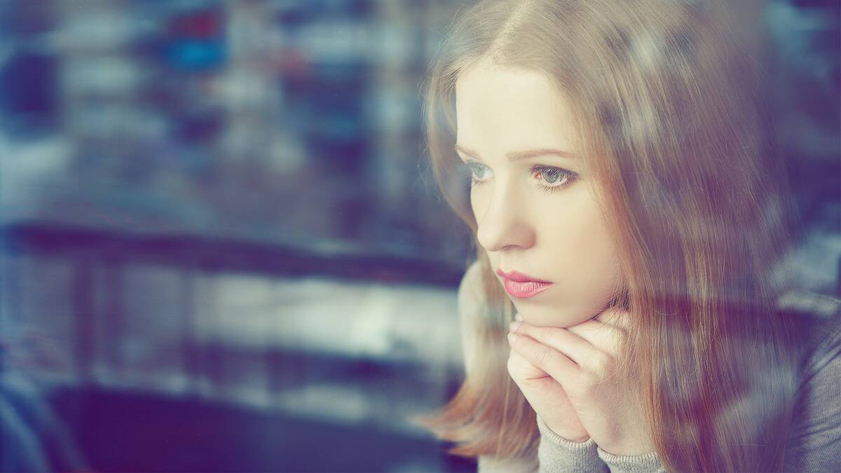 A woman leaning her chin on her folded hands, looking through a window.