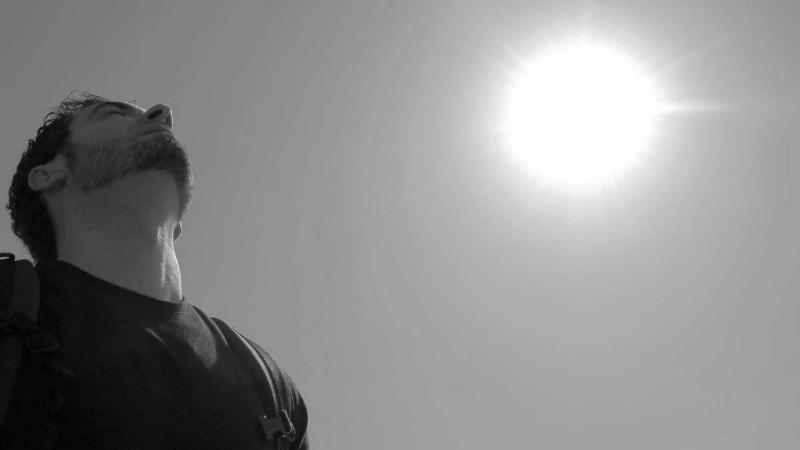 A low-angle, greyscale image of a man looking up, the sun bright behind him.