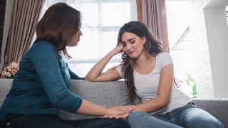 Two women sitting on the couch next to each other, one comforting the other who's clearly upset.