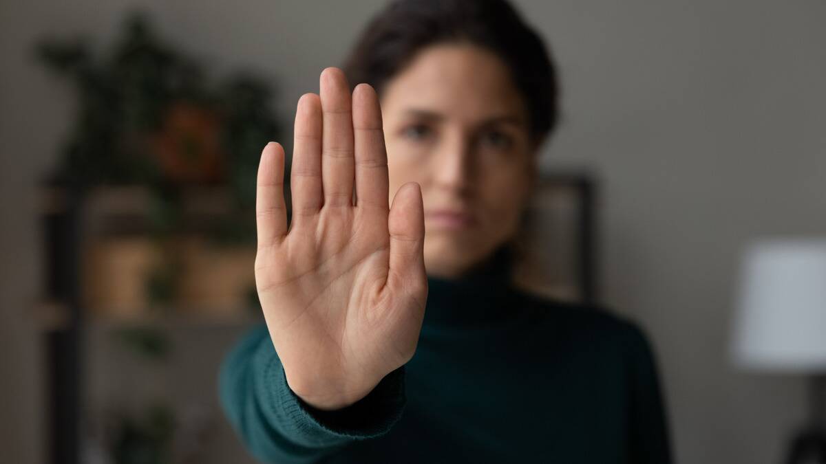 A woman holing up her hand in front of her as if saying 'no' or 'stop, her stern face visible but blurred in the background.