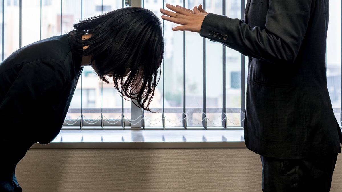 A woman bowing in apology in front of someone, the other person holding their hands out as if to say she doesn't need to.