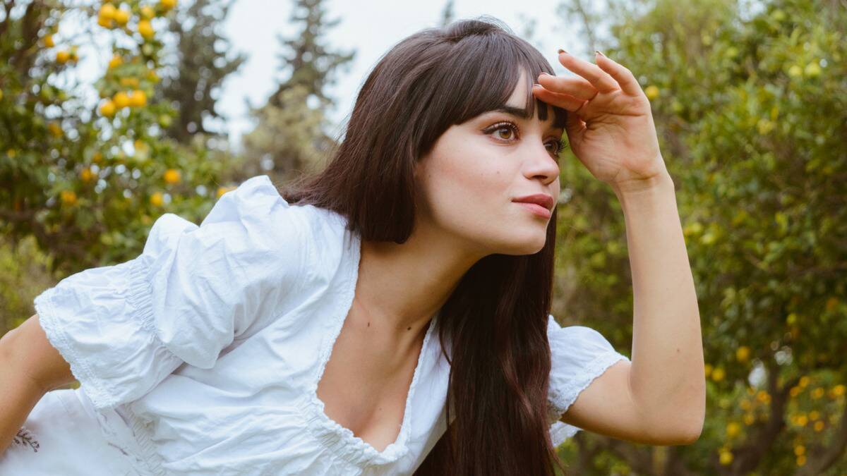 A woman leaning forward, a hand on her brow in a 'looking' gesture.