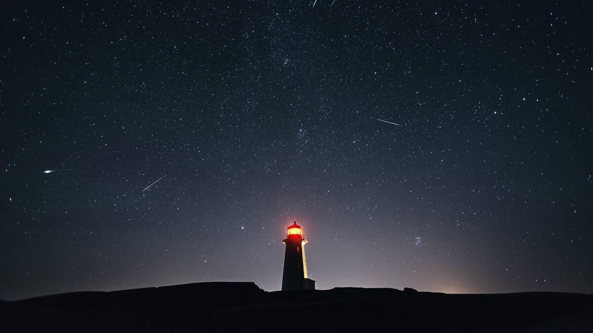 A lighthouse underneath a starry sky, a few meteors visible.